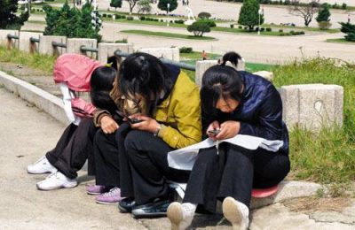 North Korean girls use their cell phones in a park.
