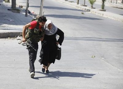 A Free Syrian Army fighter helps a woman run across a street during clashes in Aleppo. Photo by Goran Tomasevic.