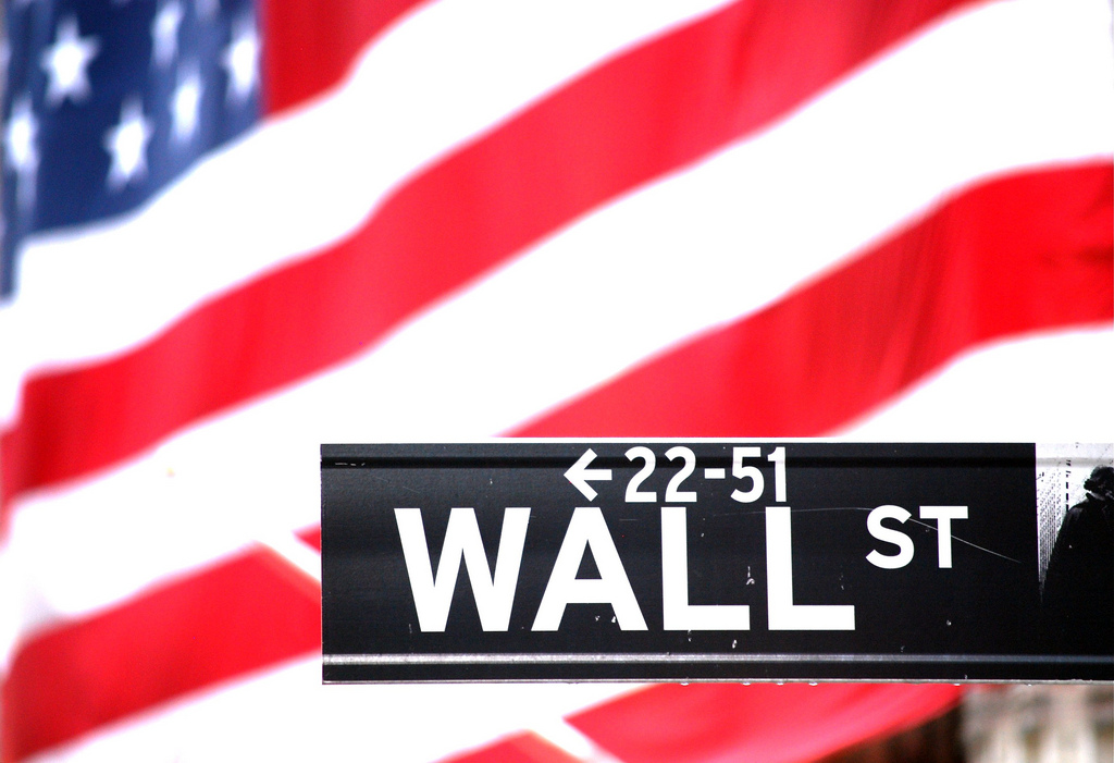 Wall Street sign with the American flag draping the columns of the New York Stock Exchange