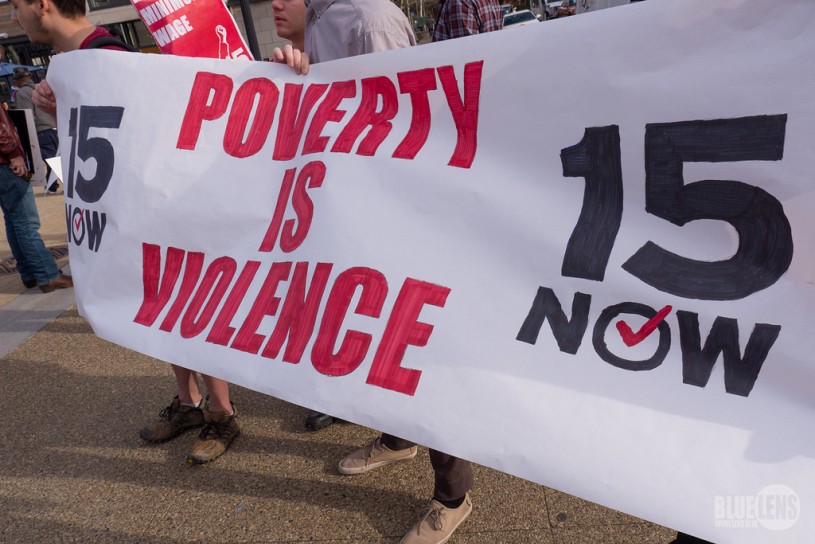 workers strike holding sign "poverty is violence - $15 now"