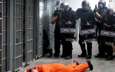 Prison guards stand over prisoner on the ground