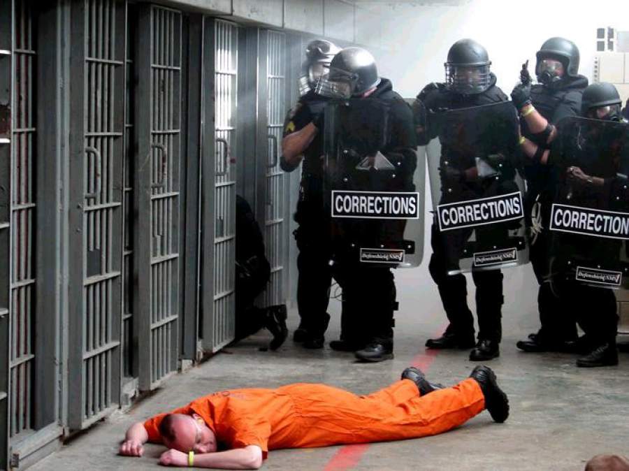 Prison guards stand over prisoner on the ground