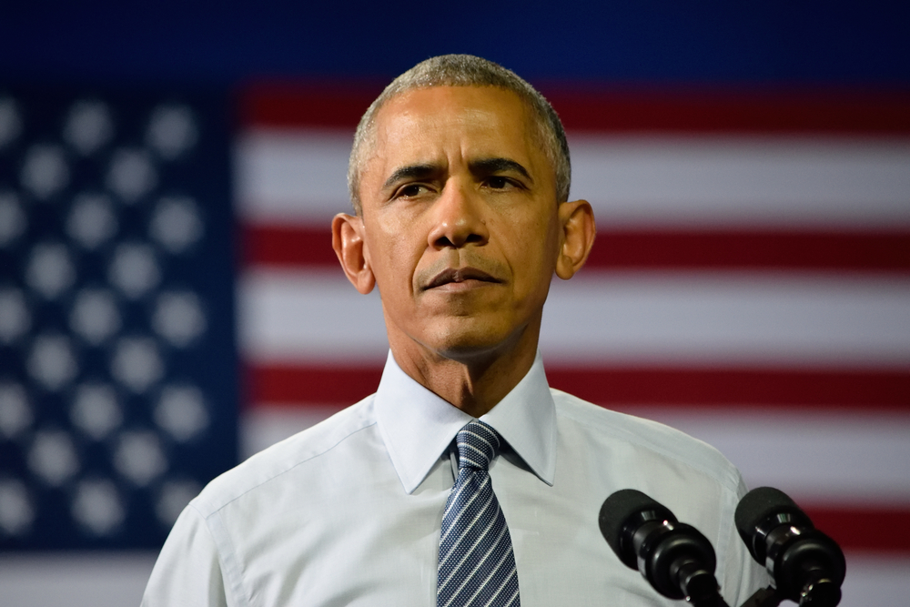 Barack Obama gazes out from behind a podium, with an American flag in the background.