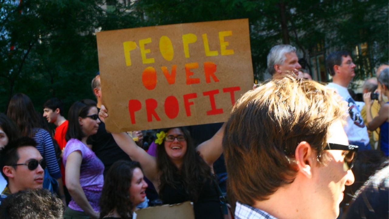 woman holding a sign that reads people over profit in regard to the coronavirus stimulus bill