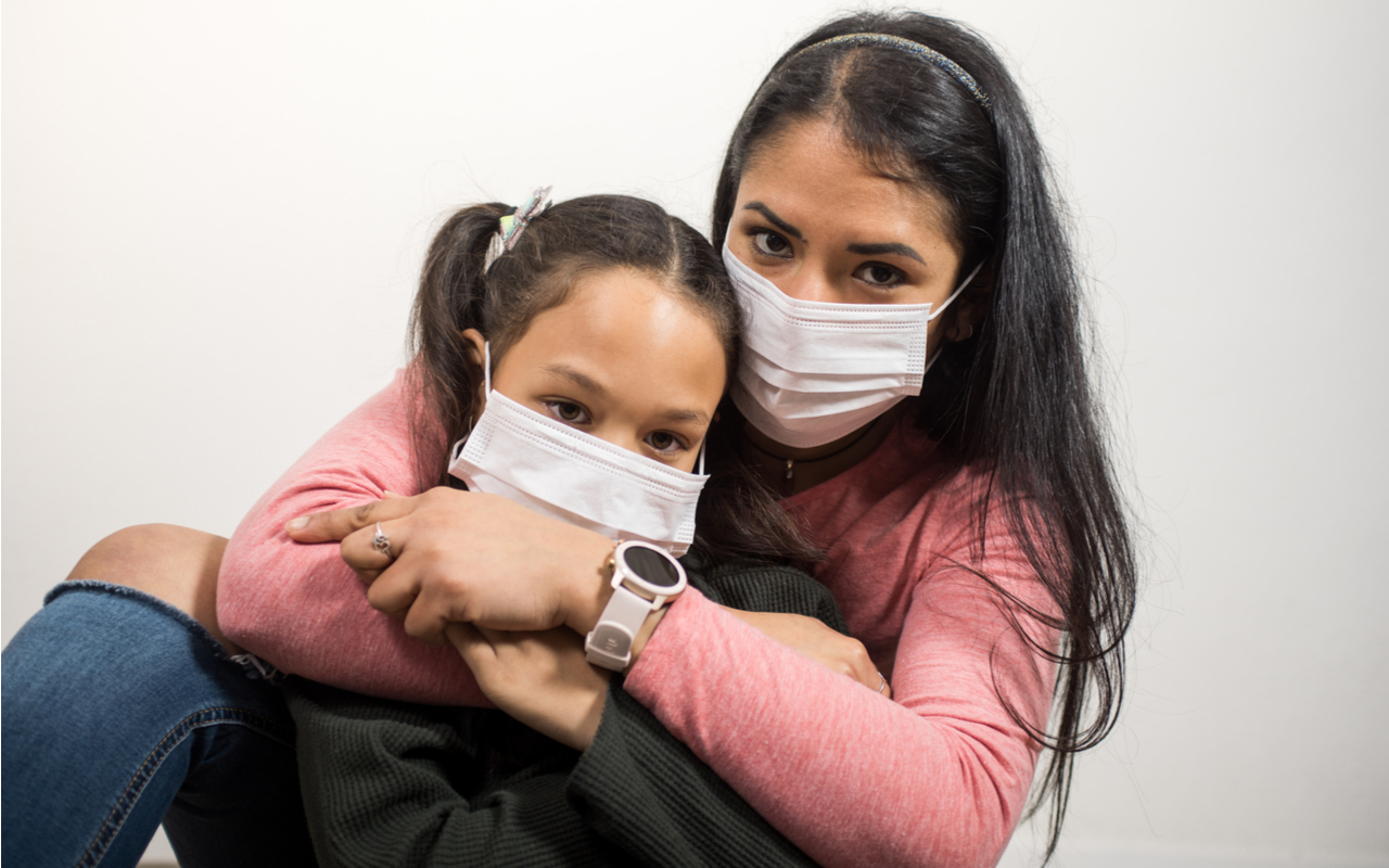 Latina mother and daughter hug each other and wearing medical masks for fear of COVID-19