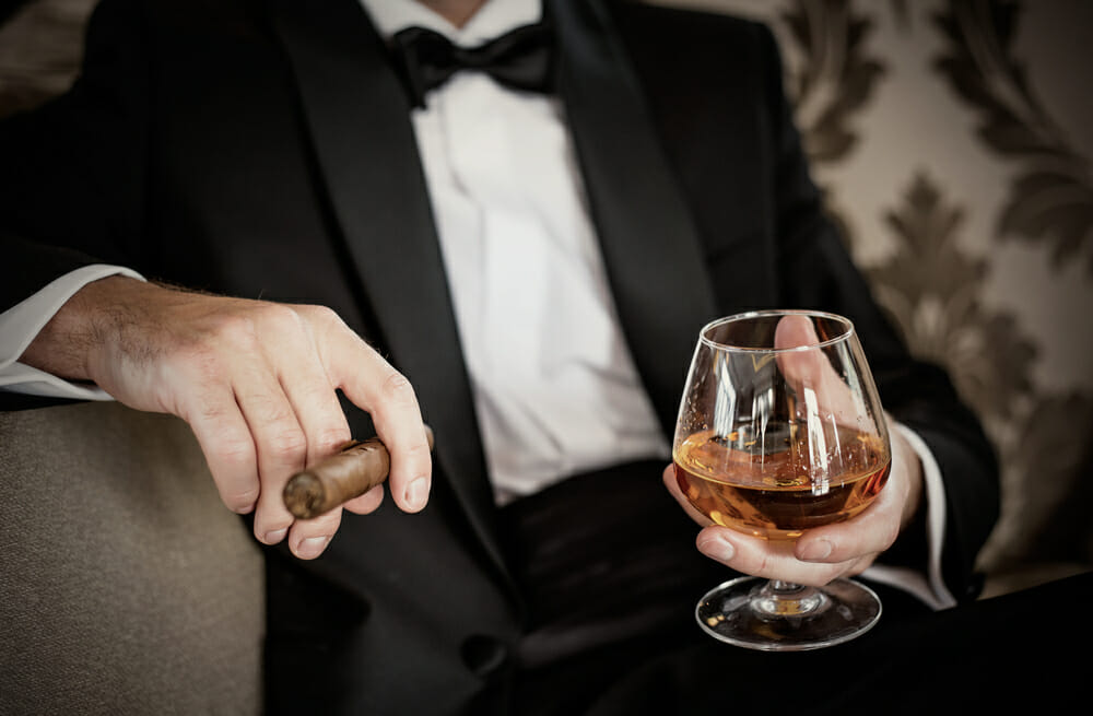 wealthy person in a suit holding a cigar and a glass of expensive liquor