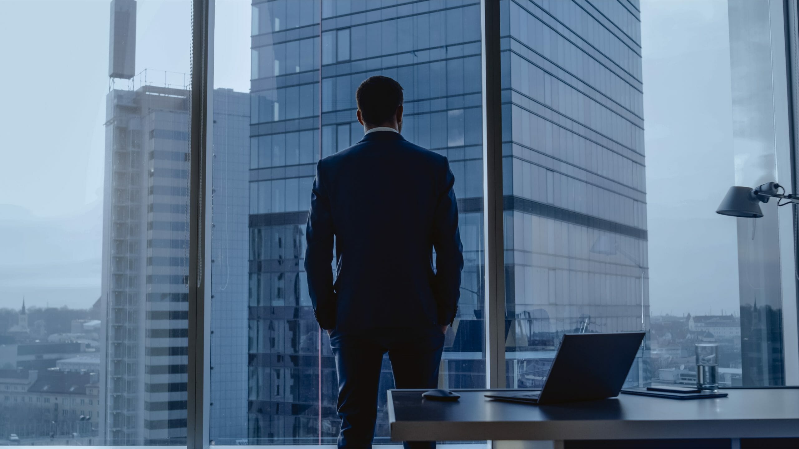 wealthy businessperson looking out the window of a high rise building