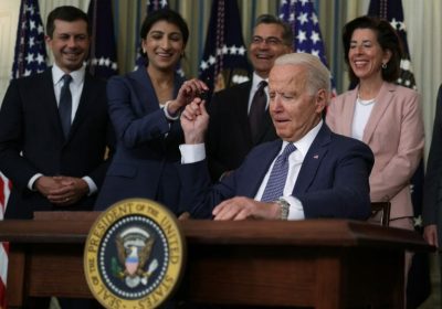 President Biden at a podium, signing an executive order to promote American economic competition, with Federal Trade Commission members behind