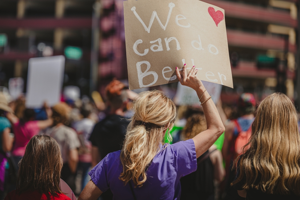 A person in a purple shirt, holding a sign that reads "We can do better" at a pro-choice march.