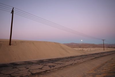 An image of desert in the northern part of California around dusk. in the foreground is small road with power lines running parallel to it.