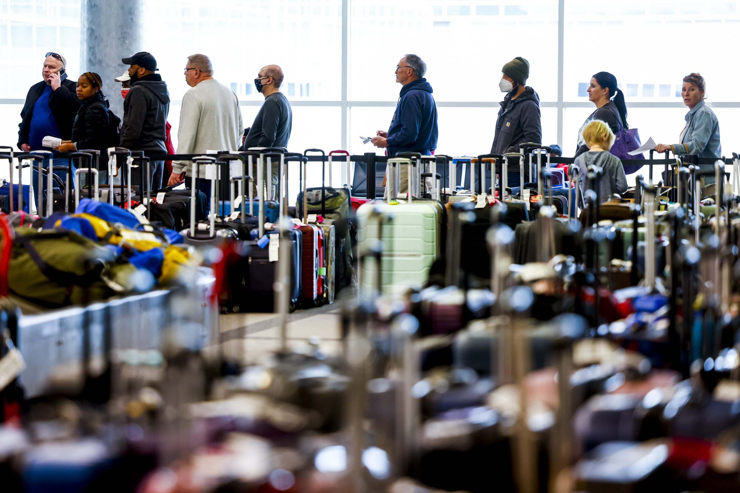 Hundreds of rolling luggage carriers filling an airline terminal, with a line of people in the background.