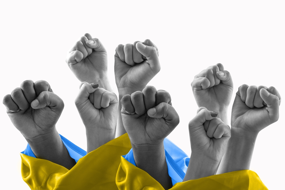 gray scale fists reaching up through a Ukrainian flag