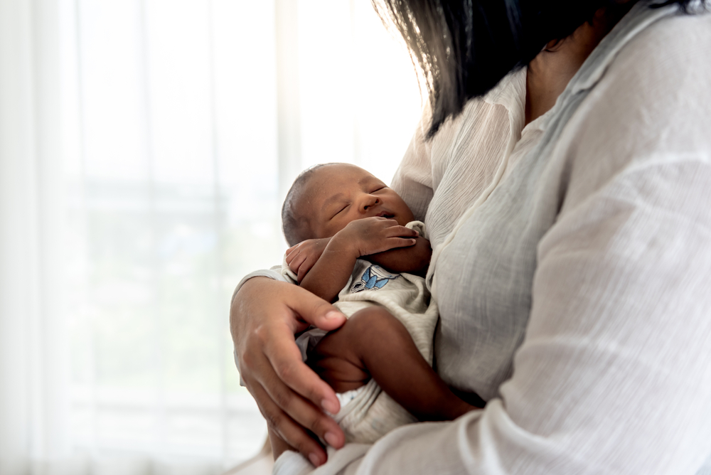 Black mother wearing a white linen shirt, cradling her child in her arms.