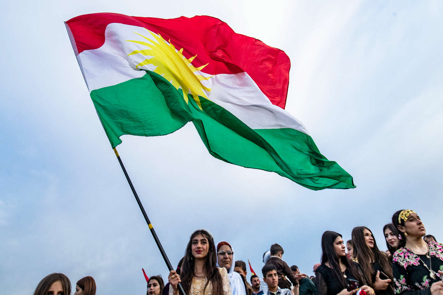 Image of Kurdish people holding up their flag at the Kurdish New Year celebration.