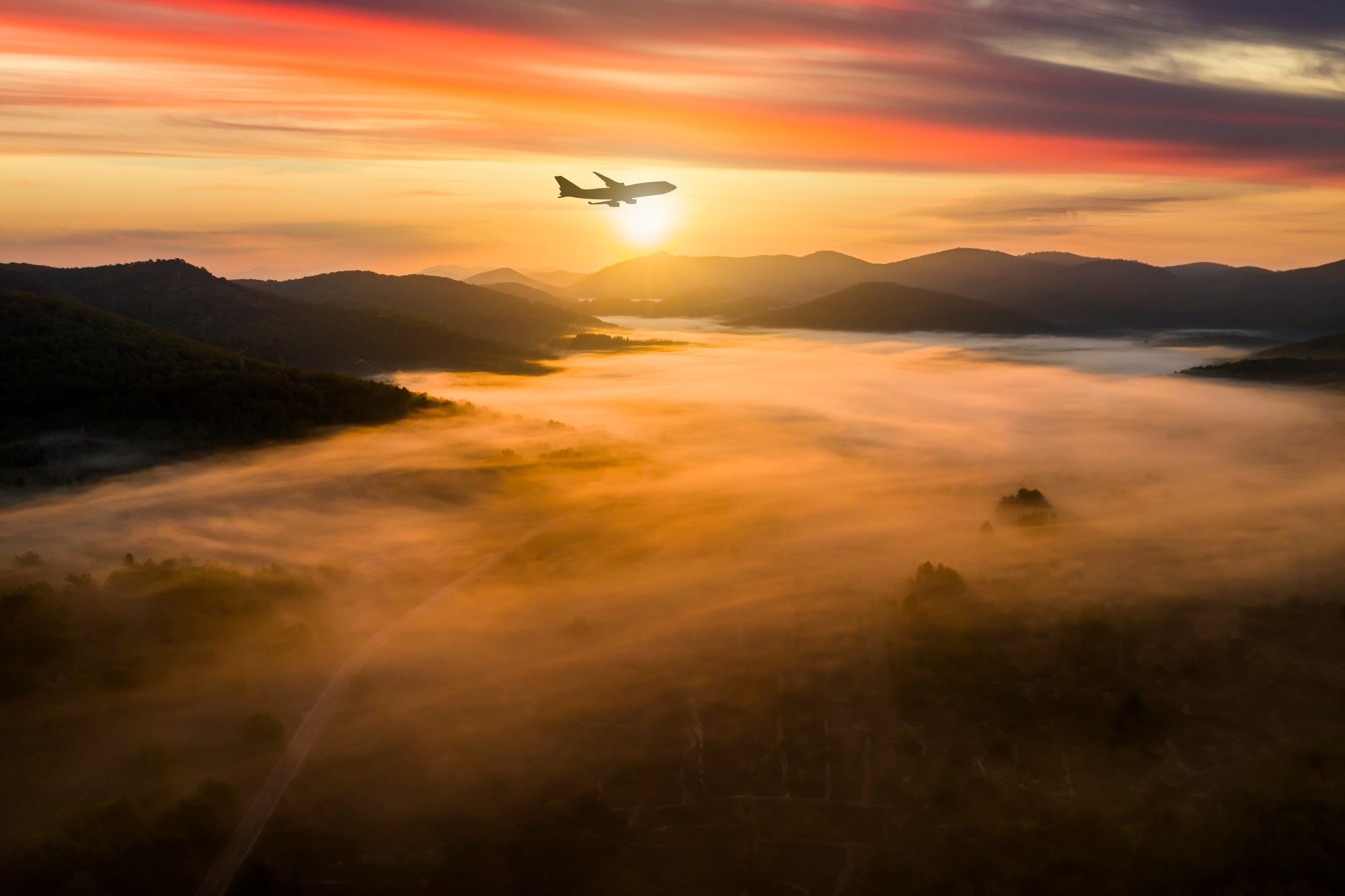 Airplane over misty mountains at dawn