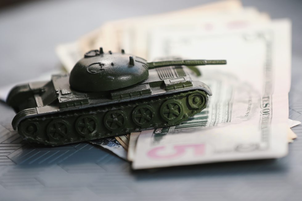 close-up shot of a toy tank sitting atop a stack of money